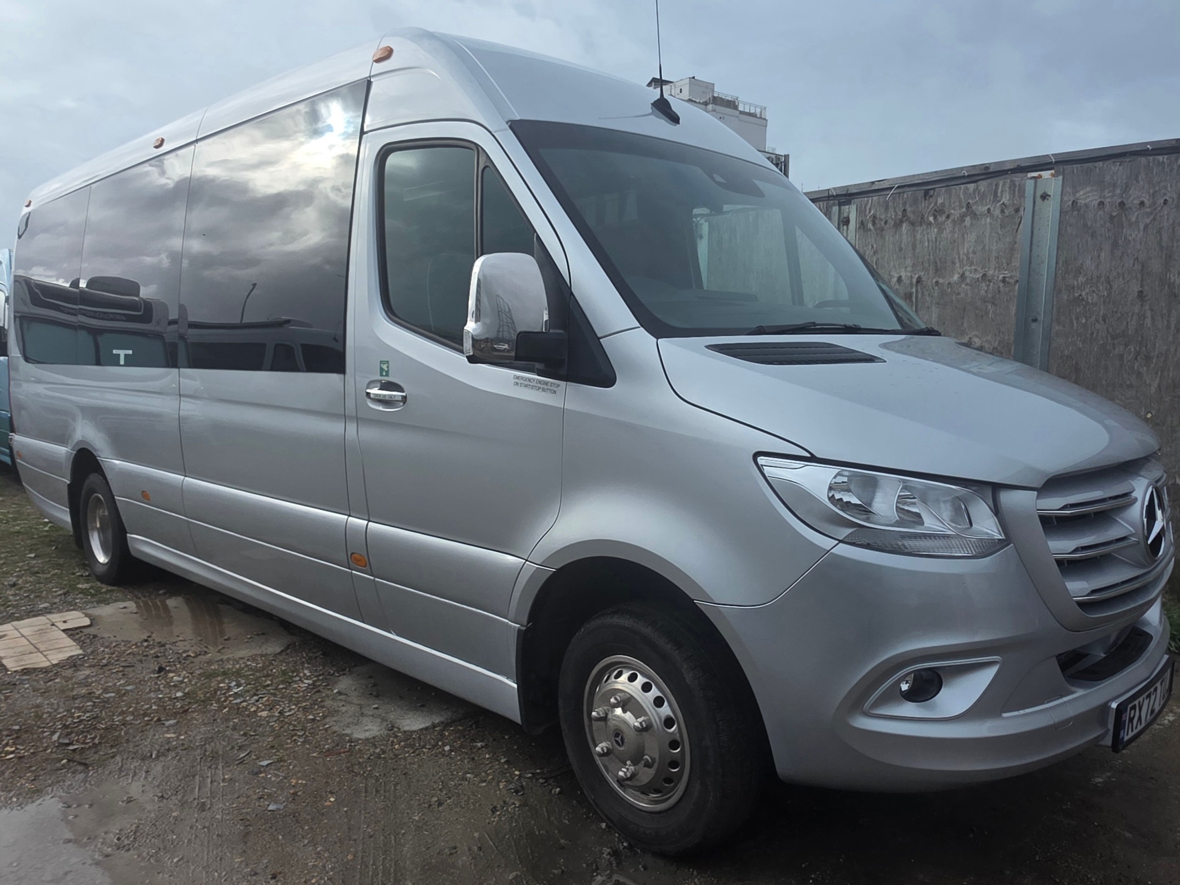 Silver Mercedes-Benz van parked on gravel with cloudy sky.