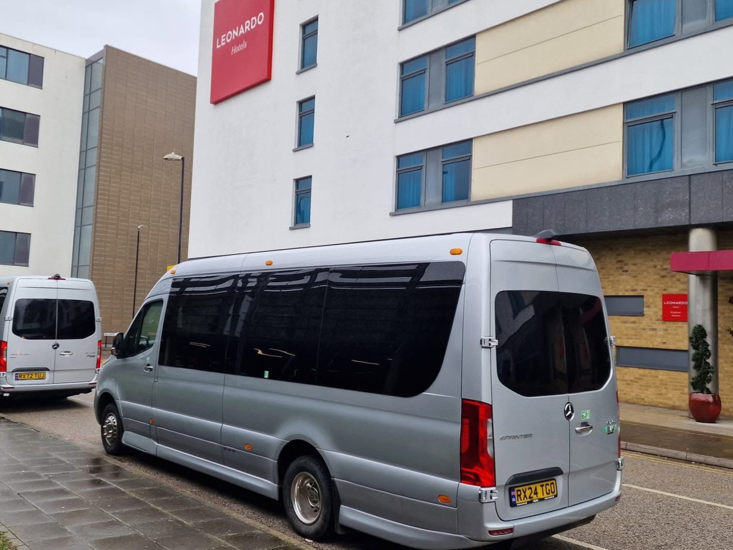Two silver minibuses parked outside a modern building with 'Leonardo Hotels' signage.
