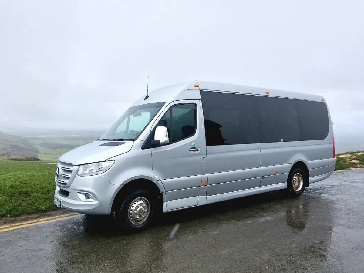 Silver van parked on a wet road with grassy hills in the background on a cloudy day.