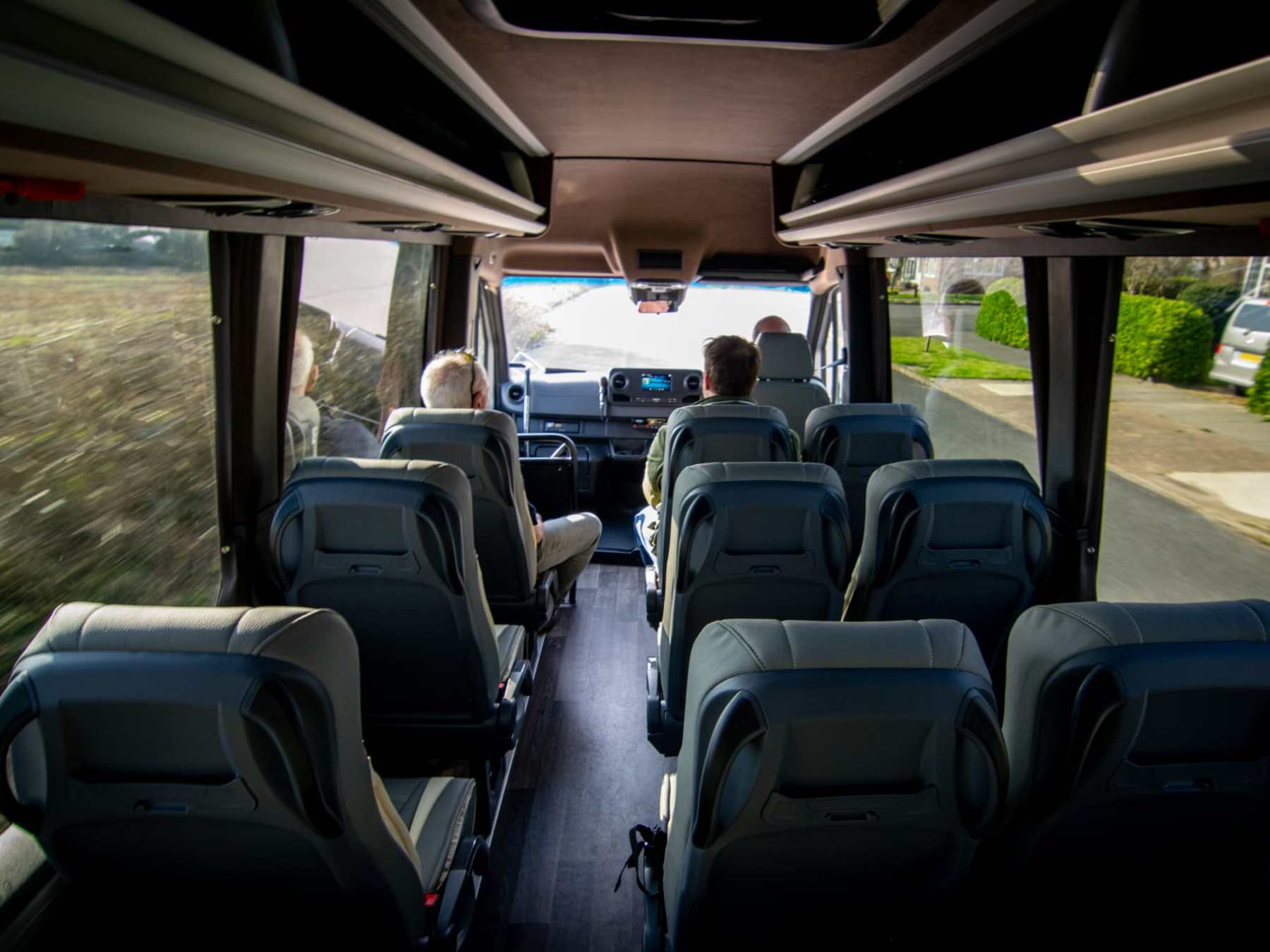 Interior of a minibus with empty seats and two passengers at the front.
